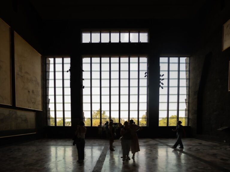Silhouette of visitors inside Mexico City's National Museum with large windows in the background.