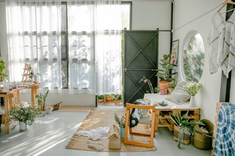 Wooden furniture on light floor with carpets near window with curtains and potted plants in light cozy room