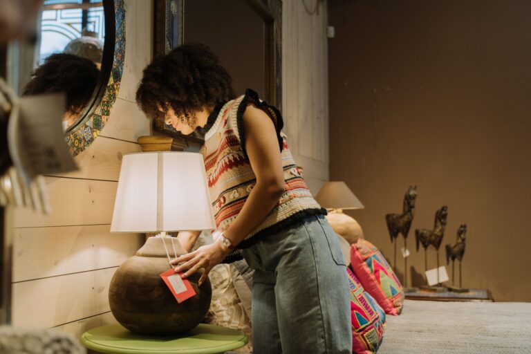 A woman examines a lamp in a cozy retail store setting with decorative elements.
