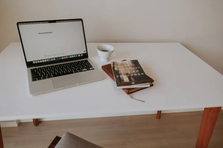 A clean, minimalist workspace with a laptop, book, and coffee on a white table.