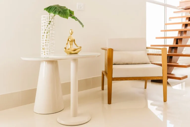 Comfortable chair placed near small white table and stylish wooden stairway in light room