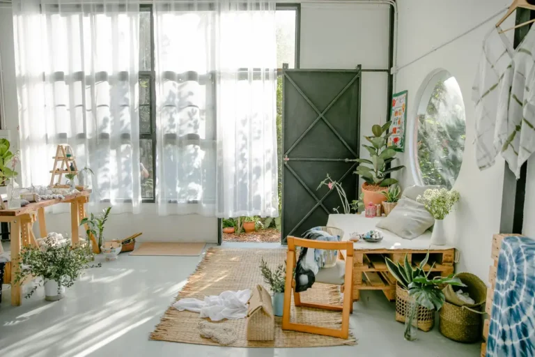 Wooden furniture on light floor with carpets near window with curtains and potted plants in light cozy room