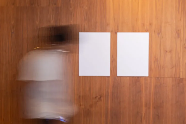 Side view of unrecognizable blurred person in motion strolling along wooden wall with white mock up placard in light room