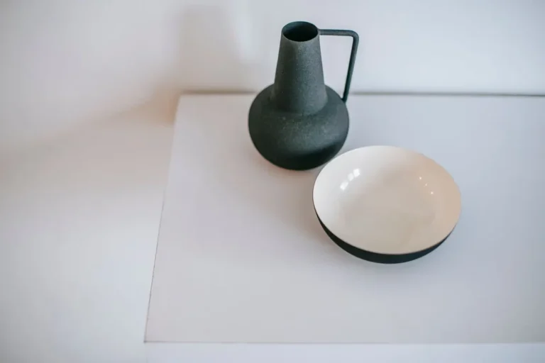 From above of empty vase with handle near round shaped bowl on white desk at home